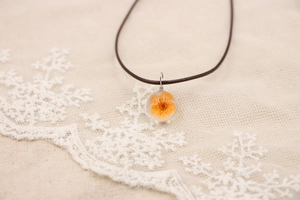 Vue détaillée du pendentif fait main avec fleur orange pressée dans une résine claire