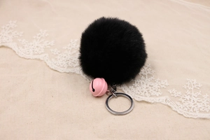 Close-up of fluffy black faux rabbit fur pom pom keychain with a small pink bell charm
