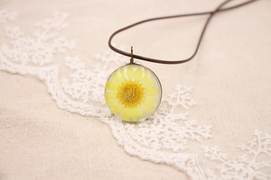 Détail du pendentif marguerite avec fleur séchée en résine sur dentelle blanche