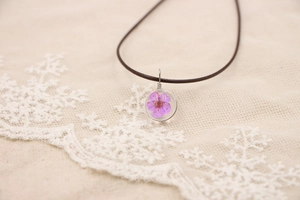 Vue détaillée du pendentif en résine avec fleur séchée sur fond en dentelle
