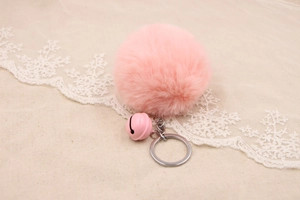 Detailed close-up of fluffy pink faux fur pompom keychain with a matching small bell charm