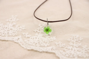 Détail d'un collier pendentif sphère avec une véritable fleur séchée verte à l'intérieur
