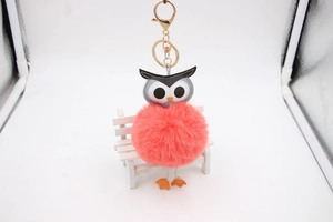 Détail du porte-clés hibou en peluche rose avec mousqueton doré sur mini banc