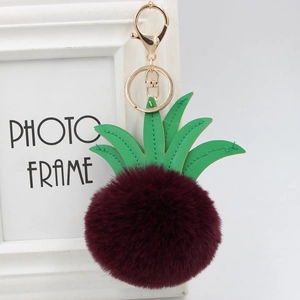 Macro detail of wine red faux fur pineapple pom-pom keychain with green PU leaves