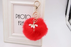 Close-up of red faux fur pompom keychain featuring a rhinestone ballerina pendant detail