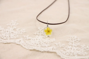 Macro d'un pendentif boule en verre fait main avec fleur séchée jaune sur cordon brun