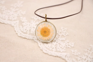 Vue détaillée d'un pendentif rond vintage avec une véritable fleur séchée orange sur dentelle