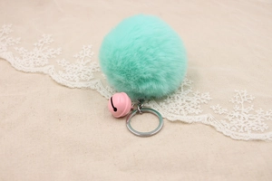 Detail of mint green faux fur pompom keychain with a pink bell and silver metal ring