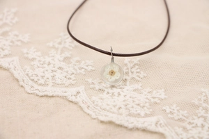 Détail d'un pendentif en résine fait main avec fleur séchée sur un cordon marron