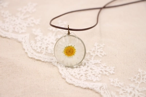Gros plan d'un pendentif en résine fait main avec une vraie marguerite et un cordon marron