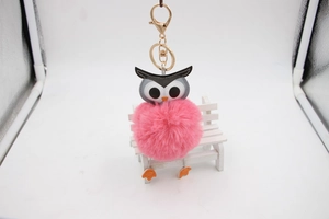 Détail d'un porte-clés chouette en fausse fourrure rose sur un petit banc blanc