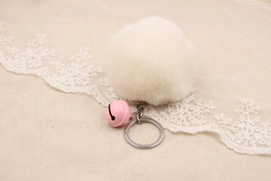 Close-up of soft white faux fur pompom keychain with a cute pink bell and silver ring
