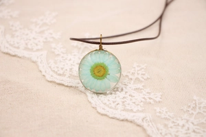 Détail macro d'une marguerite bleu clair pressée à la main dans un pendentif en bronze vintage