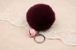 Detail of burgundy faux fur pompom keychain with a pink bell on lace fabric