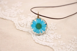 Détail d'un pendentif rond en résine avec marguerite bleue séchée sur lin beige
