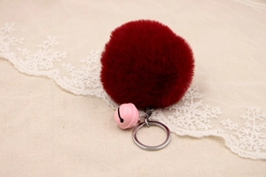 Detail of a fluffy burgundy faux fur pompom keychain with a pink bell and silver ring