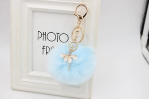 Detail of blue faux fur pompom with rhinestone ballerina charm on a gold keychain