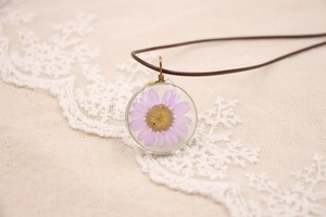Détail d'un pendentif marguerite violette sur cordon marron sur tissu de dentelle beige