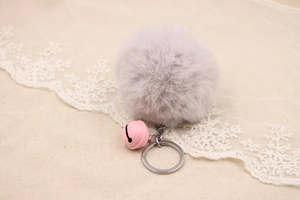 Detail of soft faux fur pompom keychain with a small pink bell and silver metal ring