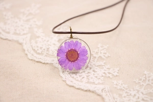 Vue détaillée d'un pendentif en résine avec marguerite violette sur cordon marron