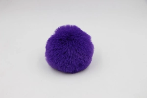 Detailed view of a soft fluffy faux rabbit fur pom pom in deep purple for bag accessories