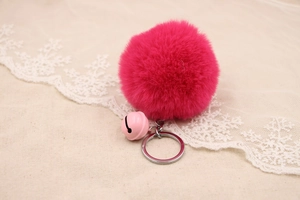 Detail of rose red faux fur pompom keychain with a pink bell on beige linen fabric