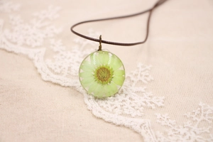 Gros plan d'un pendentif rond en résine avec une véritable fleur de marguerite verte
