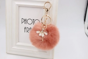 Detail of pink faux fur pompom keychain with gold ballerina pendant and flower skirt