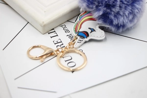 Close-up of a purple faux fur ball unicorn keychain with golden metal ring and lobster clasp