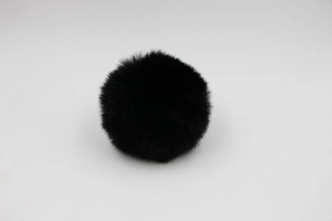 Close-up of soft black faux fur pom pom with dense synthetic fibers for bag accessories