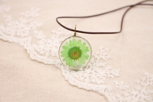 Macro d'une fleur de marguerite verte séchée dans un pendentif en résine avec cordon