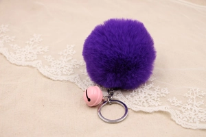 Close-up of fluffy purple faux fur pompom keychain with pink bell and silver ring details