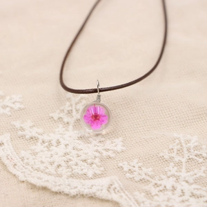 Détail macro du pendentif globe en résine avec une véritable fleur séchée rose incluse