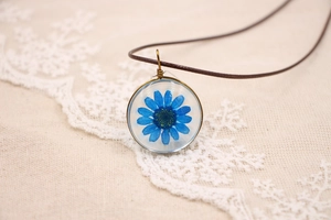 Gros plan d'un pendentif avec une fleur séchée bleue et un cadre en métal bronze antique