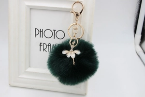 Detail of a dark green faux fur pompom keychain with a rhinestone ballerina pendant