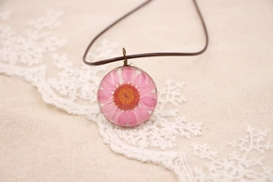 Détail d'un pendentif fleur séchée marguerite rose sur un cordon tressé marron