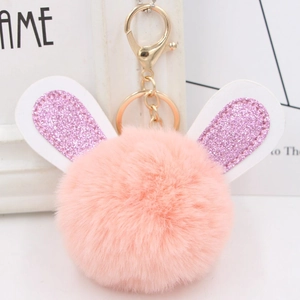 Close-up of pink fluffy pom-pom keychain with glittery purple rabbit ears and gold clasp