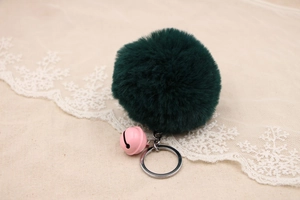 Close-up of deep green faux fur pompom keychain with a small pink bell and silver ring