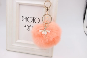 Detail of coral plush faux fur pompom with golden ballerina dancer charm and key ring
