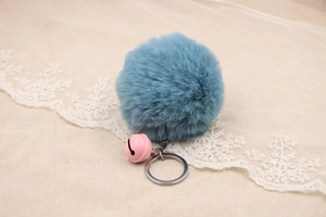 Close-up of a blue fluffy faux rabbit fur pompom keychain with a pink bell charm