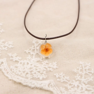 Macro d'un pendentif transparent fait main avec fleurs séchées orange et cordon brun