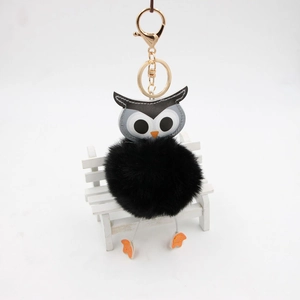 Détail d'un porte-clés hibou noir en peluche avec fermoir doré sur un mini banc blanc