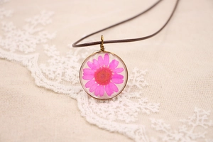 Vue macro d'un pendentif en résine avec une marguerite rose et bordure en métal bronze