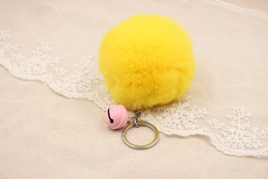 Close-up of a fluffy yellow faux fur pompom with a pink bell and silver keychain ring