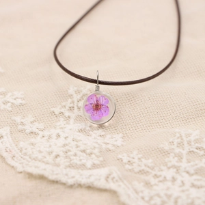 Gros plan détaillé d'un pendentif en résine fait main avec une fleur séchée violette réelle