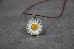Vue macro d'un collier pendentif en résine avec marguerite blanche et cordon marron