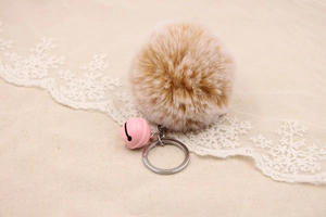 Detail of khaki faux fur pompom keychain with a pink bell and silver metal ring