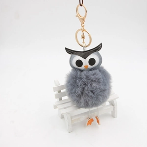 Détail du porte-clés pompon hibou gris avec fermoir doré sur un mini banc blanc élégant