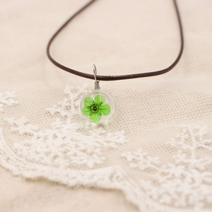 Détail d'un pendentif boule en résine avec fleur séchée verte et cordon en cuir brun