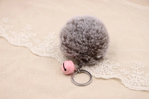 Detail of fluffy grey-brown faux fur pom-pom with pink bell and silver metal keychain